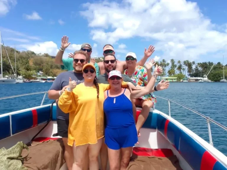 Group of guests waving on board a Real Deal boat in a palm-lined bay, Saint Lucia